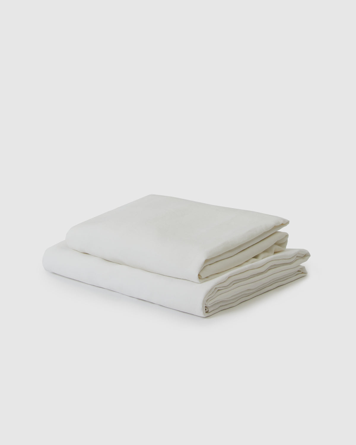 Side angle shot of creamy white milk flat and fitted sheet set
