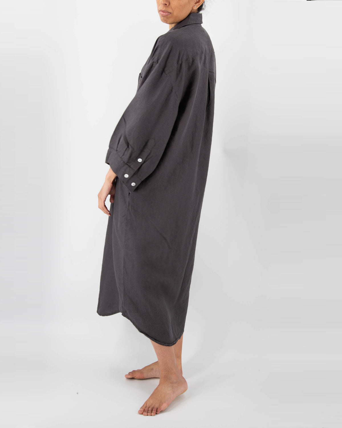 Side profile of model with full-length linen dress with buttons and front pocket in charcoal black