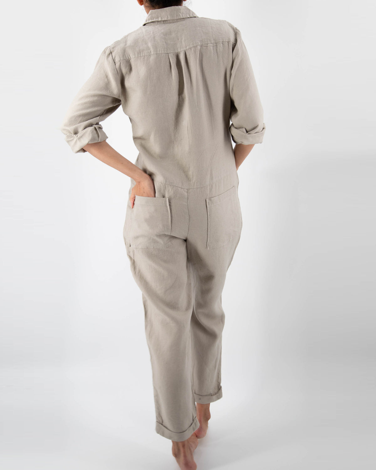 Photo of back of model in taupe linen jumpsuit with hand in back pockets