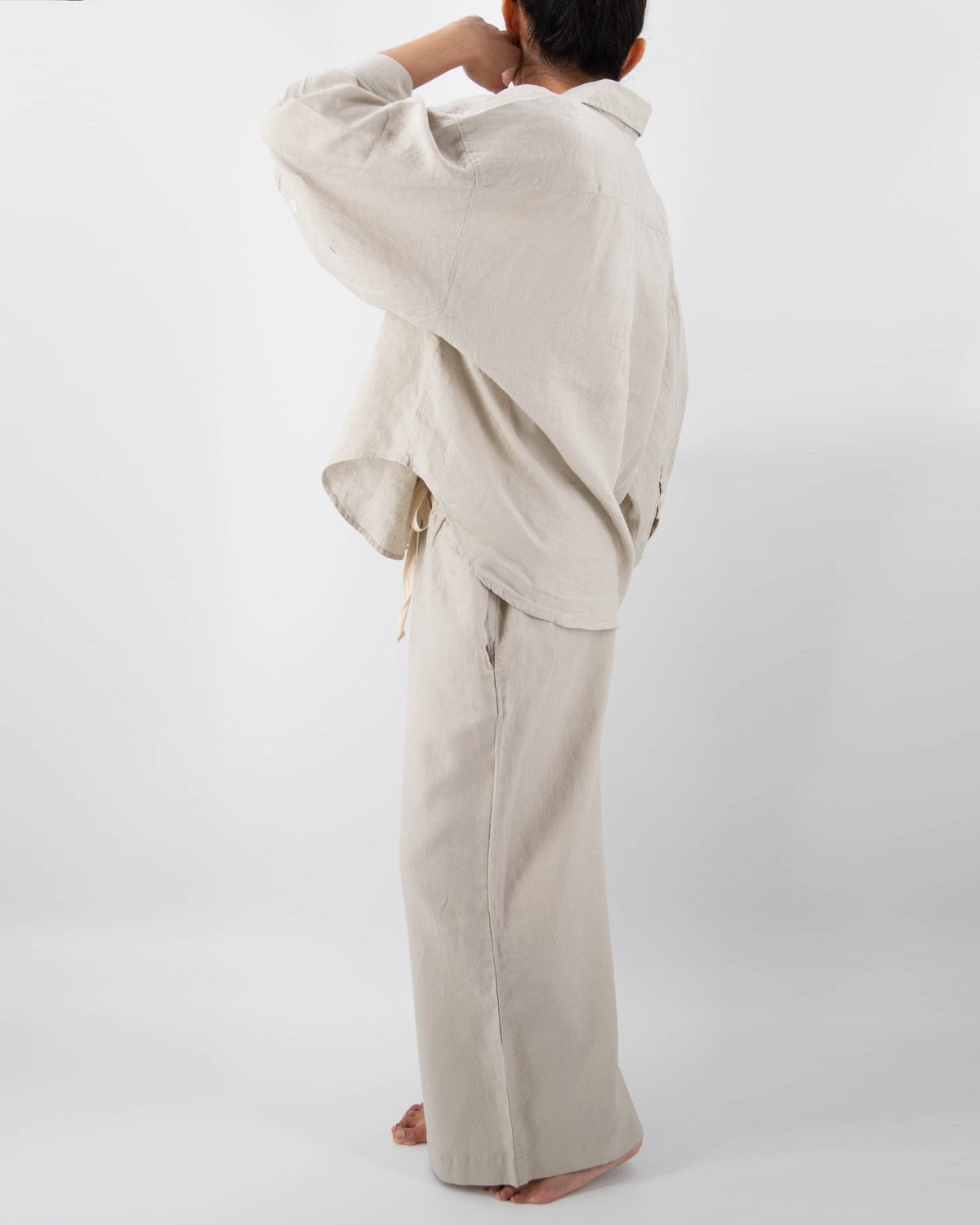Side photo of model in dove gray linen pajamas (long sleeved shirt and long pants)