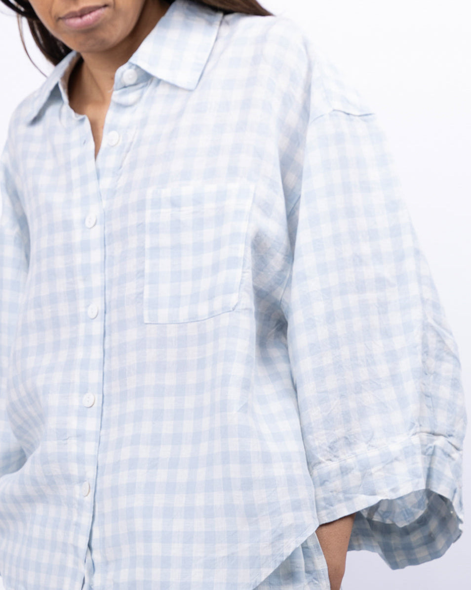 Person wearing a light blue checkered shirt and pants on a white background