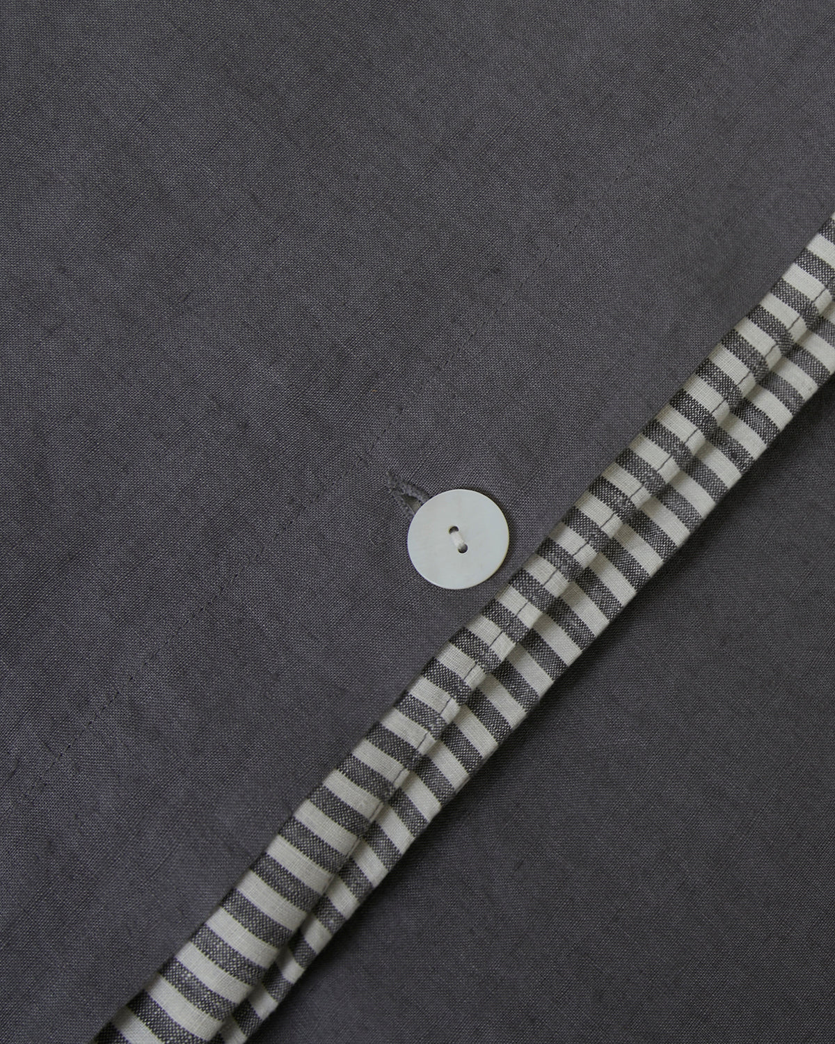 Close-up shot of storm dark gray and storm stripe linen duvet cover with mother of pearl button