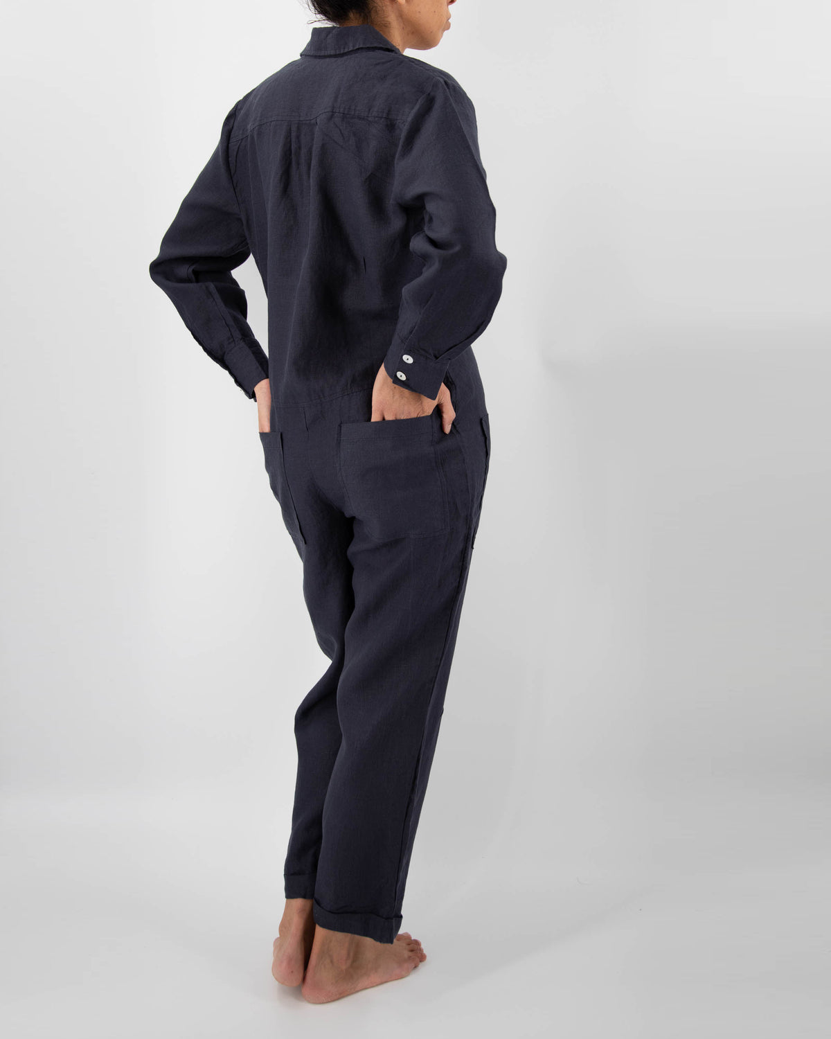 Photo of back of model in midnight blue linen jumpsuit with both hands in back pockets