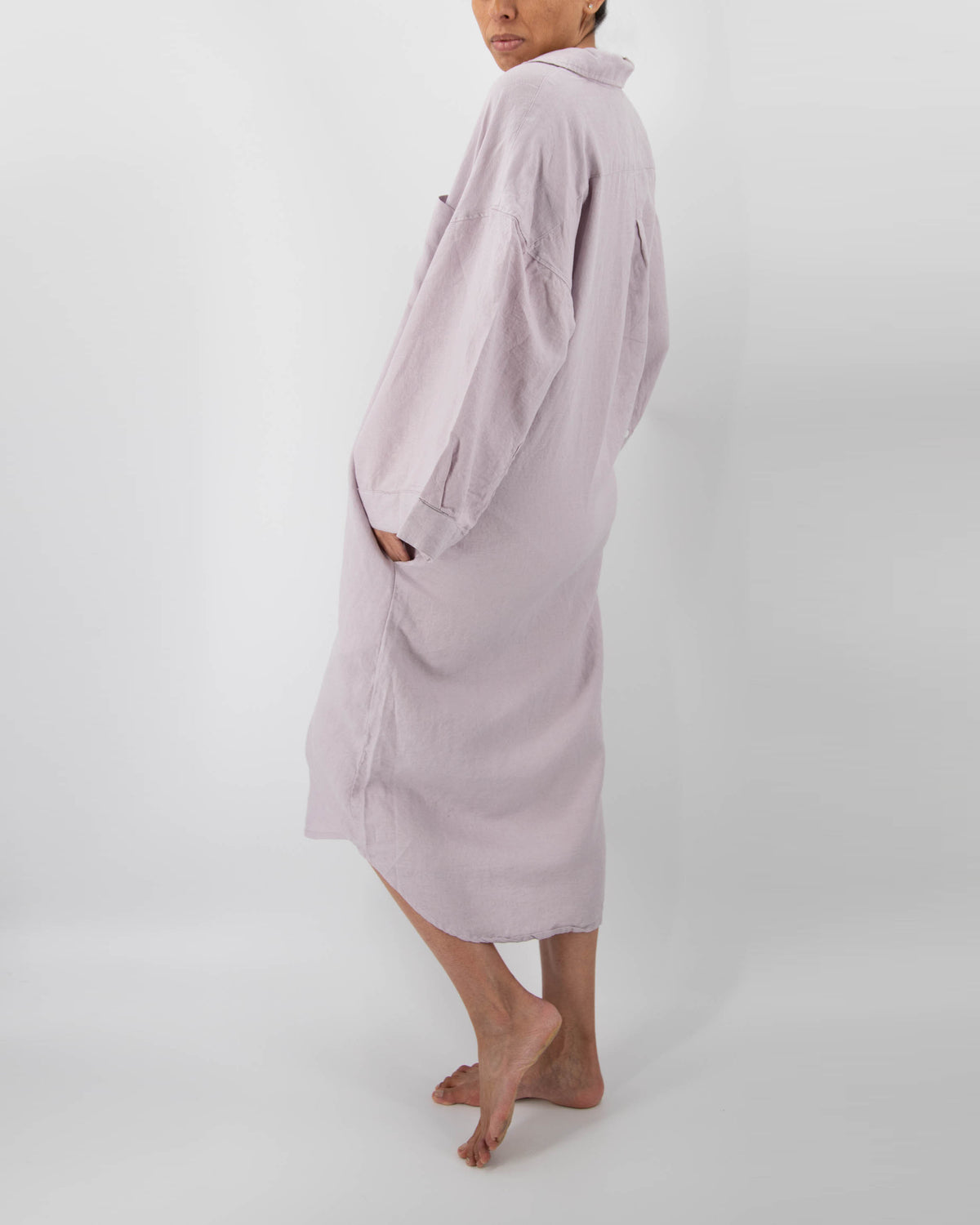 Side profile of model with full-length linen dress with buttons and front pocket in lilac purple