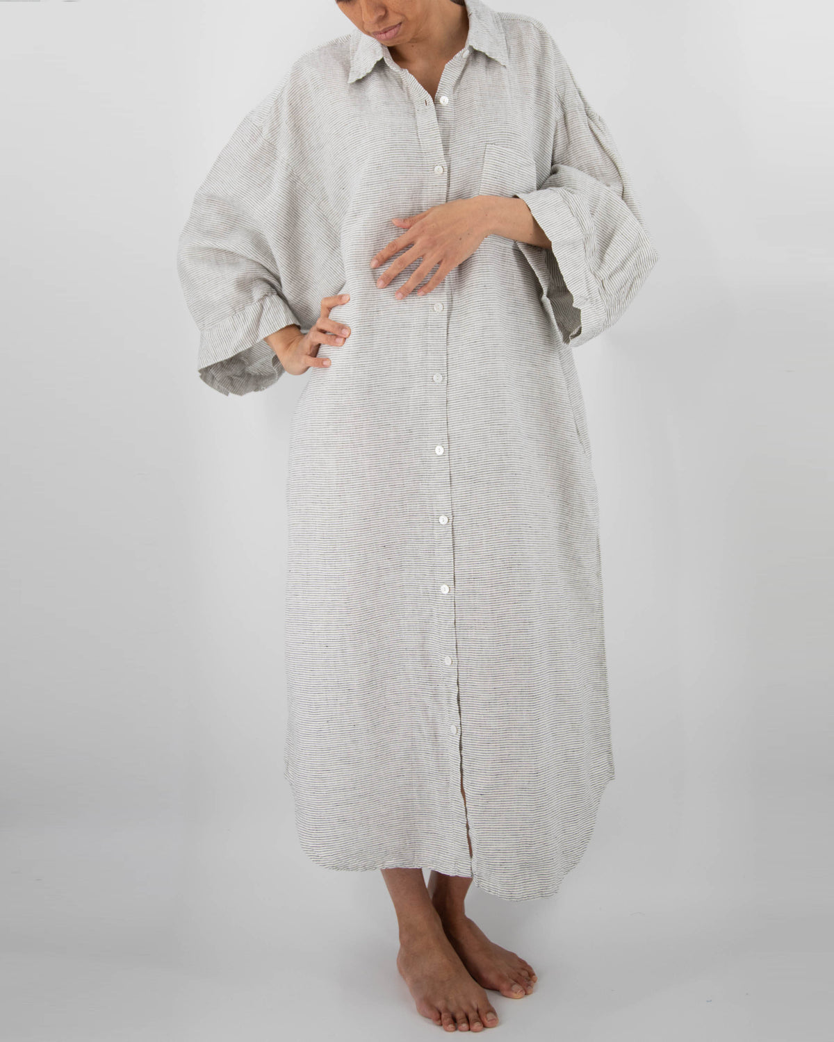 Photo of model with arm up in full-length linen dress with buttons and front pocket in pinstripe